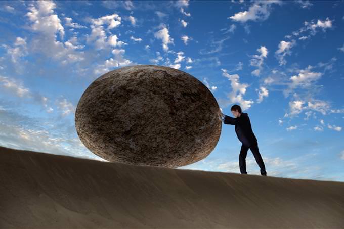 man in suit pushing a rock up a hill