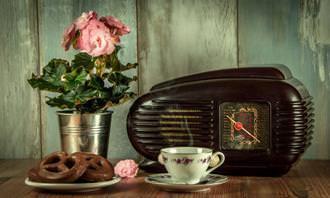 A table with a tin vase, chocolate covered pretzels, an antique teacup and radio