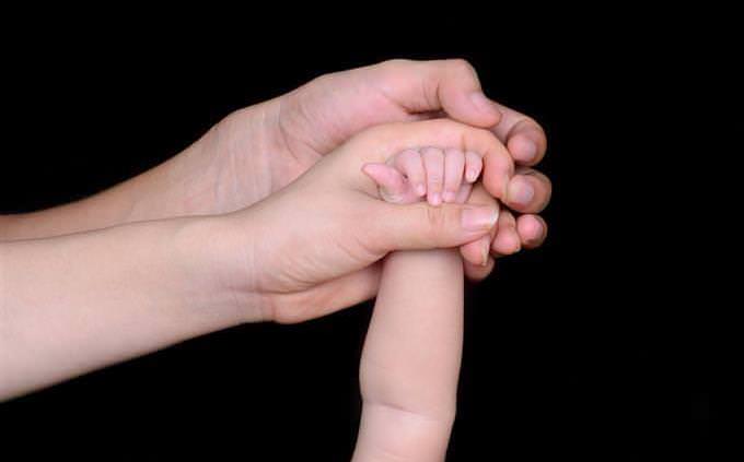 A woman's hand holding the hand of a baby