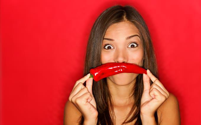 young woman holding chili pepper in front of mouth