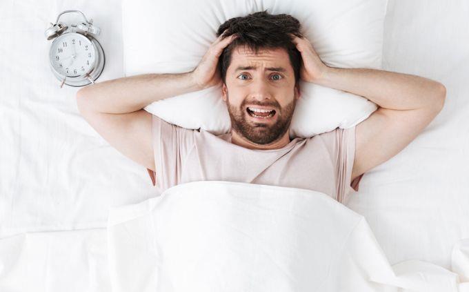 Você é um mentiroso: um homem estressado ao lado de um despertador na cama