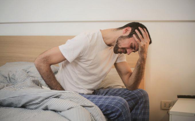 Você está cansado ou estressado: um homem sentado em uma cama segurando a cabeça